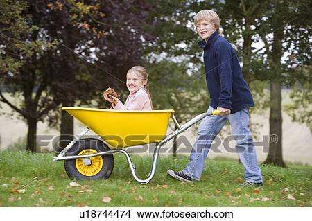 Young boy outdoors pushing young girl in wheelbarrow and smiling (selective focus) View Large Photo Image Picture - Young boy outdoors pushing young girl in wheelbarrow and smiling (selective focus). Fotosearch