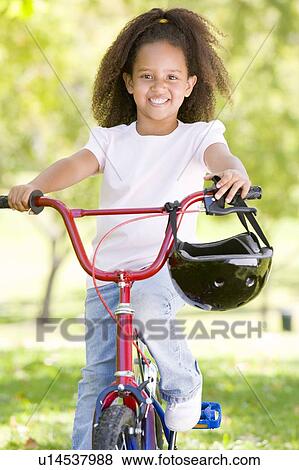 Stock Photo - Young girl on bicycle outdoors smiling. Fotosearch