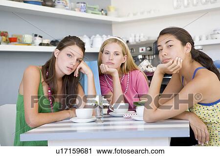 Stock Image - Three bored young women sitting at a table. Fotosearch