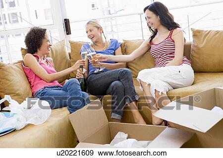 Stock Photo - Three girl friends toasting champagne by boxes in new home smiling. Fotosearch