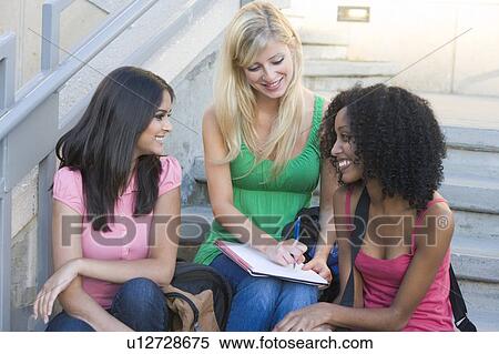 Stock Photography - Three women sitting on staircase outdoors writing in notebook. Fotosearch