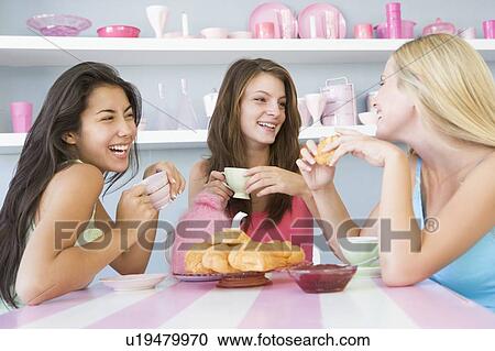 Stock Image - Three young woman sitting at a table having tea and a snack. Fotosearch