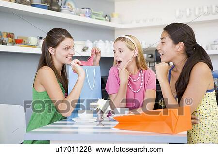 Stock Photo - Three young woman sitting at a table taking a break from shopping. Fotosearch