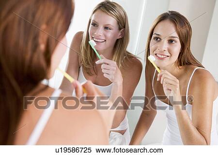 Stock Photography - Two women in bathroom brushing teeth and smiling. Fotosearch