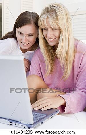 Stock Image - Two women on patio using laptop smiling. Fotosearch
