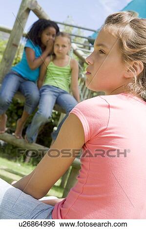 Stock Photograph - Two young girl friends at a playground whispering about other girl in foreground. Fotosearch