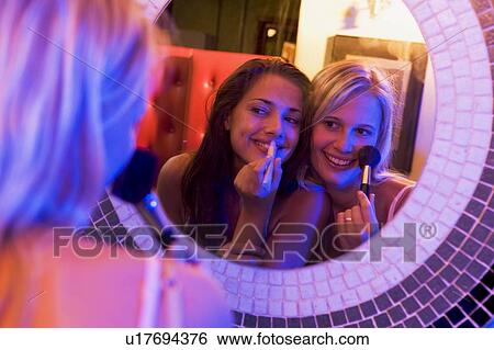 Stock Photograph - Two young women applying makeup in a mirror. Fotosearch