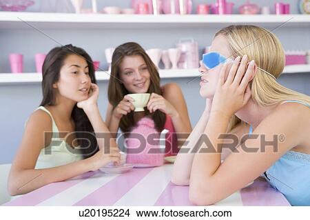 Picture - Young woman with a hangover sitting at a table with two friends. Fotosearch