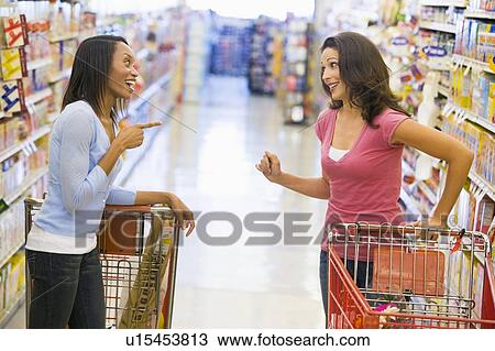 Two women talking to each other at a grocery store View Large Photo Image Stock Image - Two women talking to each other at a grocery store. Fotosearch
