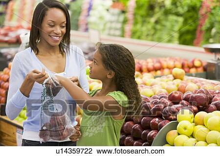 Stock Image - Woman and daughter shopping for apples at a grocery store. Fotosearch