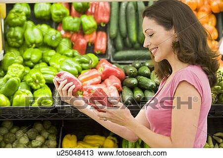 Stock Image - Woman shopping for bell peppers at a grocery store. Fotosearch