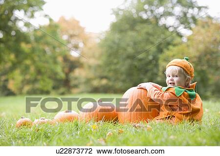 Stock Image - Baby boy outdoors in pumpkin costume with real pumpkins. Fotosearch