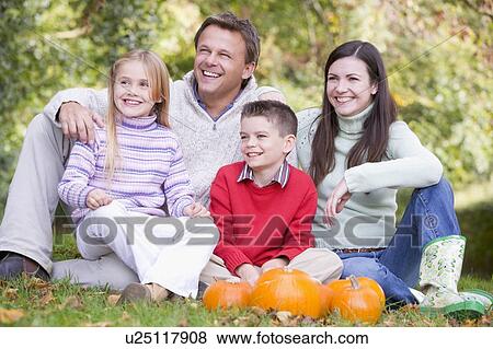 Stock Photo - Family sitting on grass with pumpkins smiling. Fotosearch