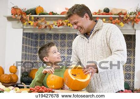 Stock Photo - Father and son carving jack o lanterns on Halloween and smiling. Fotosearch