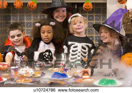 Stock Photograph - Four young friends and a woman at Halloween eating treats and smiling. Fotosearch