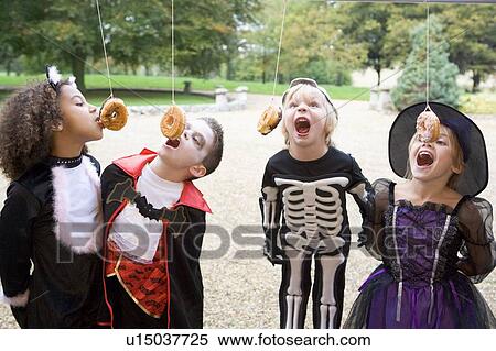 Four young friends on Halloween in costumes eating donuts hanging off strings View Large Photo Image Stock Photography - Four young friends on Halloween in costumes eating donuts hanging off strings. Fotosearch