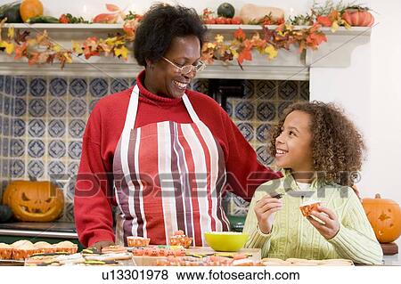 Stock Photo - Grandmother and granddaughter making Halloween treats and smiling. Fotosearch