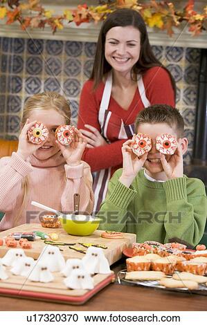 Stock Image - Mother and two children at Halloween playing with treats and smiling. Fotosearch