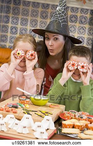 Stock Image - Mother and two children at Halloween playing with treats and smiling. Fotosearch