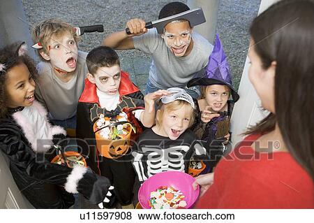 Stock Photo - Six children in costumes trick or treating at woman's house. Fotosearch
