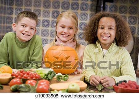 Stock Photography - Three young friends on Halloween with jack o lantern and food smiling. Fotosearch