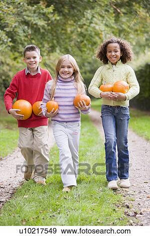 Three young friends walking on path with pumpkins smiling View Large Photo Image Stock Photo - Three young friends walking on path with pumpkins smiling. Fotosearch