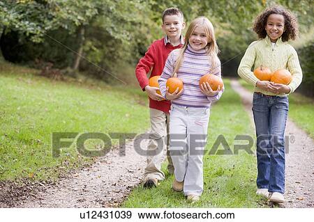 Three young friends walking on path with pumpkins smiling View Large Photo Image Stock Photo - Three young friends walking on path with pumpkins smiling. Fotosearch