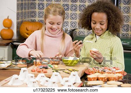 Stock Photography - Two young girl friends at Halloween making treats and smiling. Fotosearch