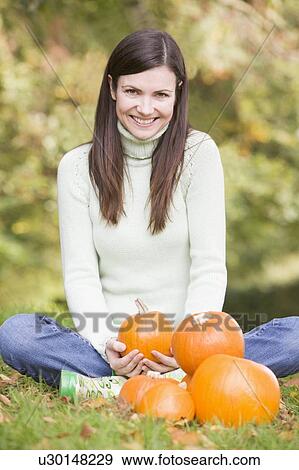Woman sitting on grass with pumpkins smiling View Large Photo Image Stock Photo - Woman sitting on grass with pumpkins smiling. Fotosearch