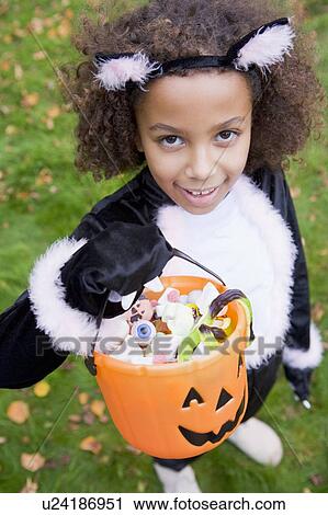 Stock Image - Young girl outdoors in cat costume on Halloween holding candy. Fotosearch