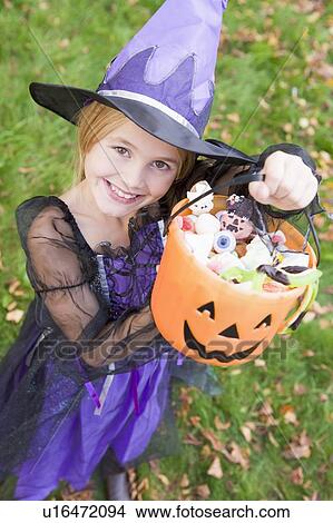 Picture - Young girl outdoors in witch costume on Halloween holding candy. Fotosearch