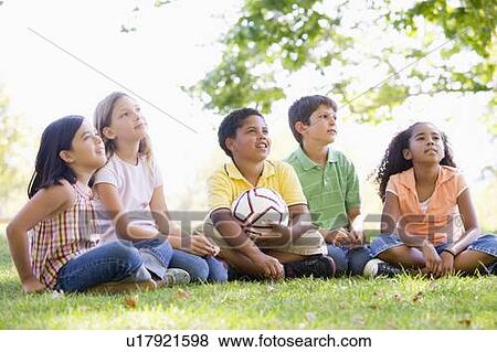 Stock Photo - Five young friends sitting outdoors with soccer ball looking up. Fotosearch