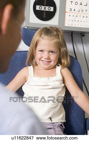 Optometrist in exam room with young girl in chair smiling View Large Photo Image Stock Photo - Optometrist in exam room with young girl in chair smiling. Fotosearch