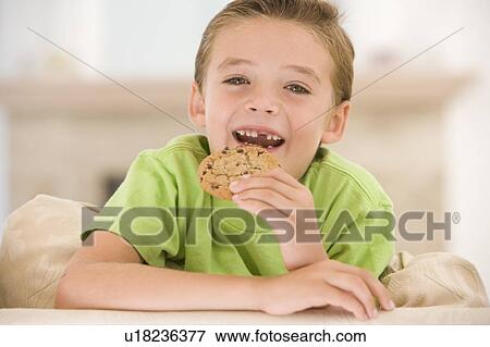Stock Photo - Young boy eating cookie in living room smiling. Fotosearch