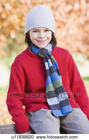 Stock Image - Young boy outdoors at park sitting on fence smiling (selective focus). Fotosearch