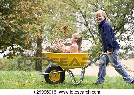 Young boy outdoors pushing young girl in wheelbarrow and smiling (selective focus) View Large Photo Image Stock Photograph - Young boy outdoors pushing young girl in wheelbarrow and smiling (selective focus). Fotosearch