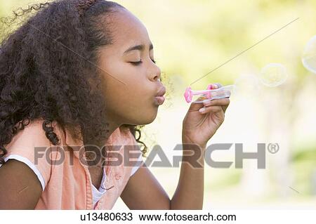 Stock Image - Young girl blowing bubbles outdoors. Fotosearch