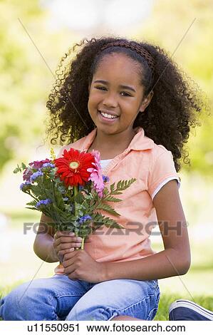 Stock Image - Young girl holding flowers and smiling. Fotosearch
