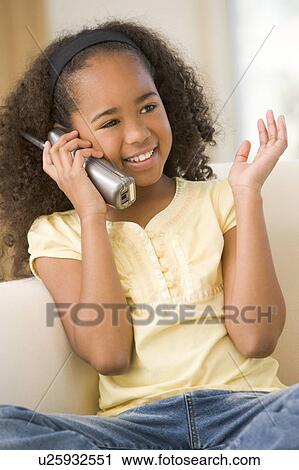 Stock Image - Young girl in living room using telephone and smiling. Fotosearch