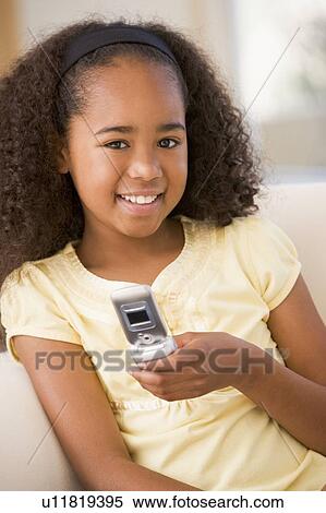 Stock Photography - Young girl in living room using cellular phone and smiling. Fotosearch