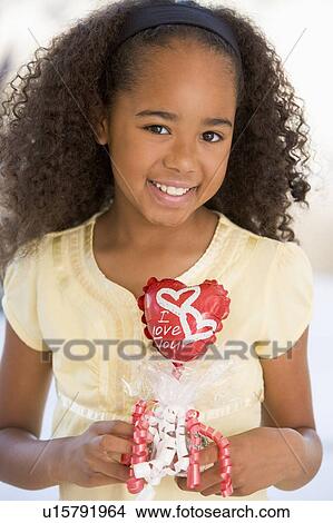 Picture - Young girl on Valentine's Day holding love themed balloon smiling. Fotosearch