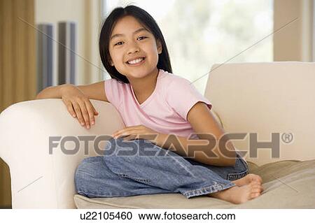 Stock Image - Young Girl Sitting On A Sofa At Home. Fotosearch