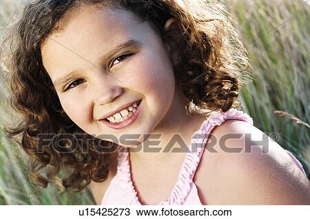 Stock Image - Young girl sitting outdoors smiling. Fotosearch