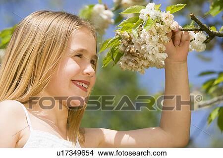 Picture - Young girl standing outdoors holding blossom smiling. Fotosearch