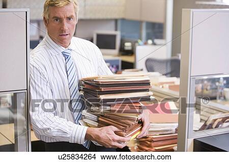 Businessman standing in cubicle holding stacks of files View Large Photo Image Picture - Businessman standing in cubicle holding stacks of files. Fotosearch