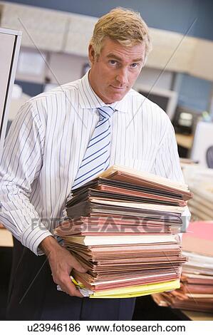 Stock Photograph - Businessman standing in cubicle with stacks of files. Fotosearch