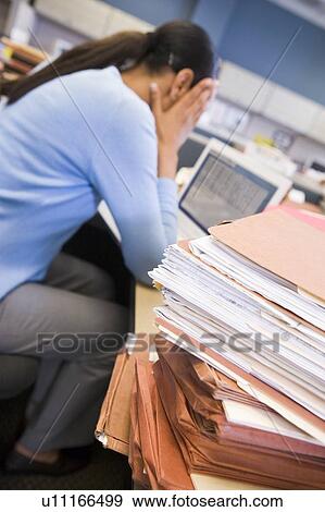 Stock Photo - Businesswoman in cubicle with laptop and stacks of files. Fotosearch