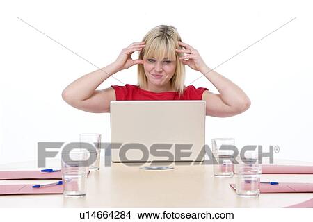 Picture - Businesswoman sitting in boardroom with laptop looking frustrated. Fotosearch