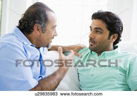 Stock Image - Two men in living room talking (high key). Fotosearch