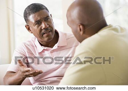 Stock Image - Two men in living room talking. Fotosearch